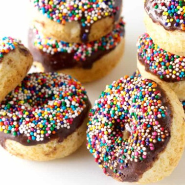 Angled view of stacked baked vanilla cake donuts topped with a semi-sweet chocolate glaze and sprinkles.