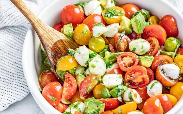 Caprese Avocado Salad in a white bowl with a wooden spoon