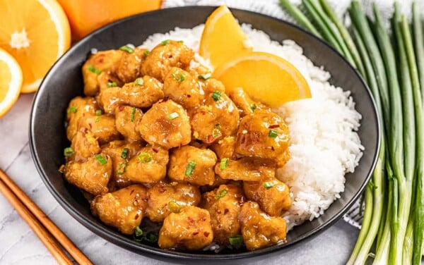 Orange chicken and rice on a black plate.