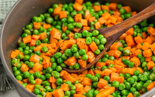 Peas and carrots in a pot with a wooden spoon.