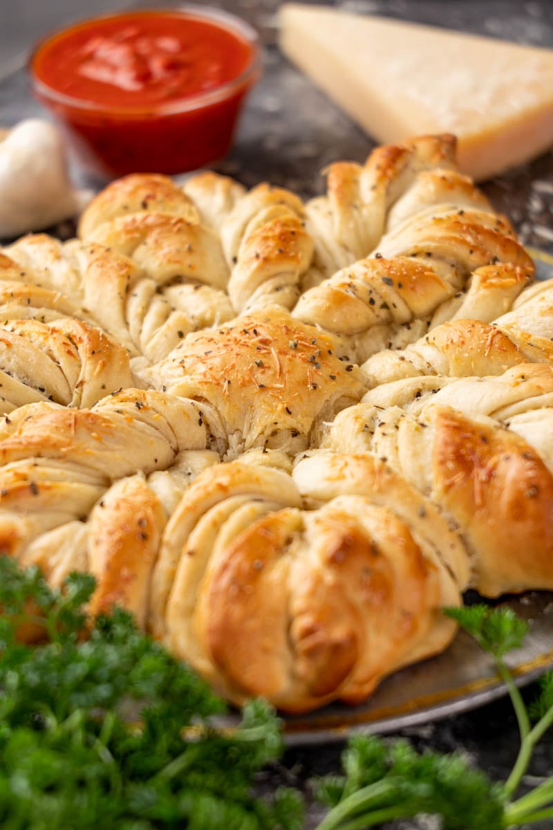 Garlic bread star bread surrounded by parsley and marinara sauce for dipping.