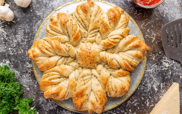 A loaf of garlic bread star bread sits on a table with a spatula and bowl of marinara sauce for dipping lay on the side.