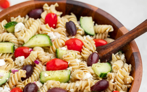 Close up view of greek pasta salad in a wood bowl.