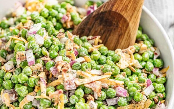 A white bowl filled with pea salad with a large wooden spoon inside