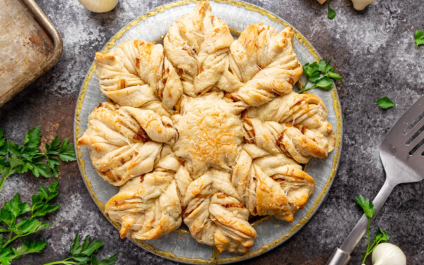 Overhead view of a loaf of Gruyere Onion Star Brea on a table surrounded by loose sprigs of flat leaf parsley.