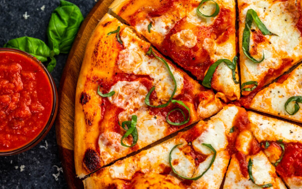 Overhead view of margherita pizza with a side small bowl filled with marinara dipping sauce.