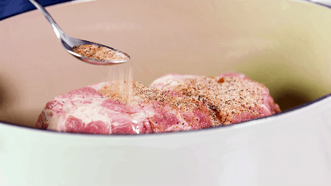 Seasoning being sprinkled over a pork roast