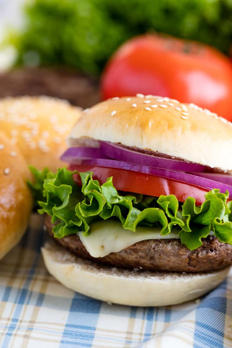 Close up of a hamburger made from homemade hamburger buns, beef, pepper jack cheese, lettuce, tomato, and onion.