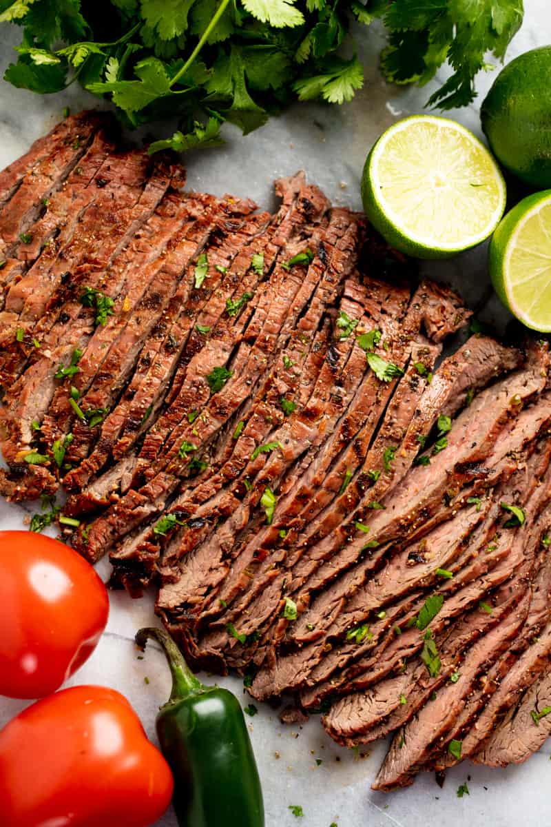 Bird's eye view of Carne Asada surrounded by limes, tomatoes, and jalapenos.