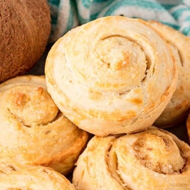 Angled view of a stack of Coconut Rolls surrounded by whole coconuts on a concrete countertop.