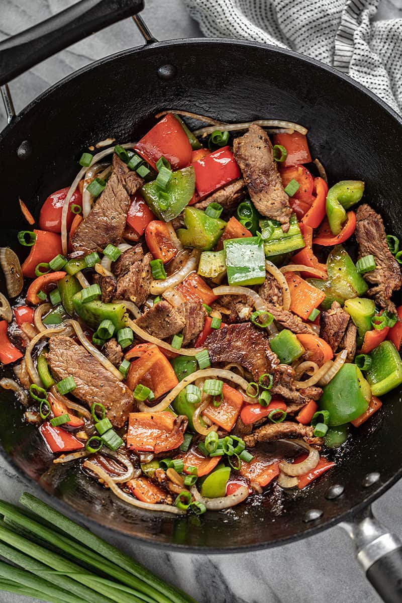 Easy Chinese Pepper Steak in a skillet with steak, red and green peppers, white onion and chopped green onion