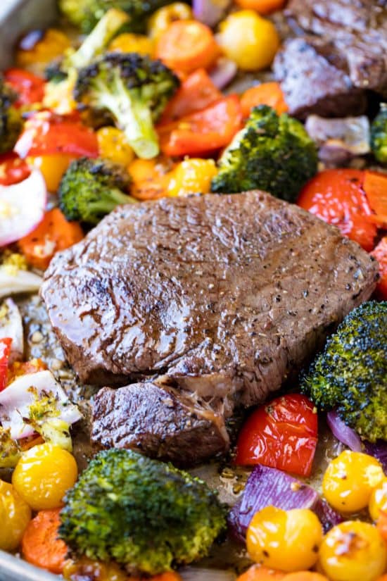 A juicy steak surrounded by roasted broccoli, cherry tomatoes, bell peppers red onion 