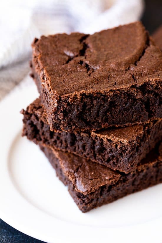 Three squares of the most amazing brownies stacked on top of each other on a white plate