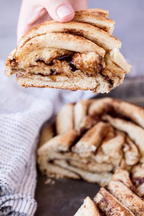 Rachel lifts a slice of Cinnamon Roll Twist Bread, revealing the layers of cinnamon sugar filling