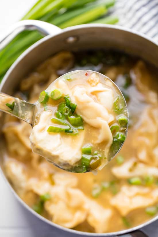 A ladle of Wonton Soup with wontons and green onion