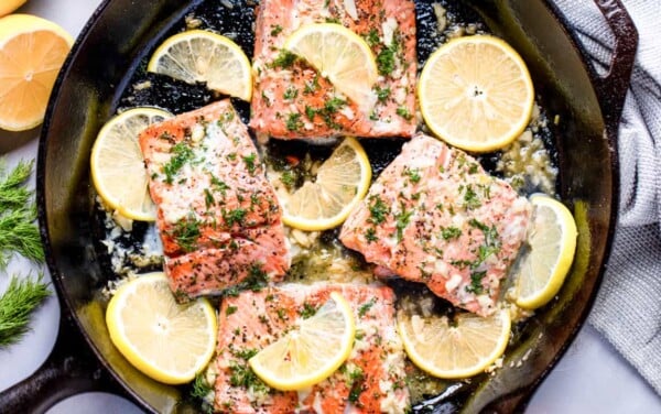 Overhead view of Salmon in a skillet surrounded by lemon slices.