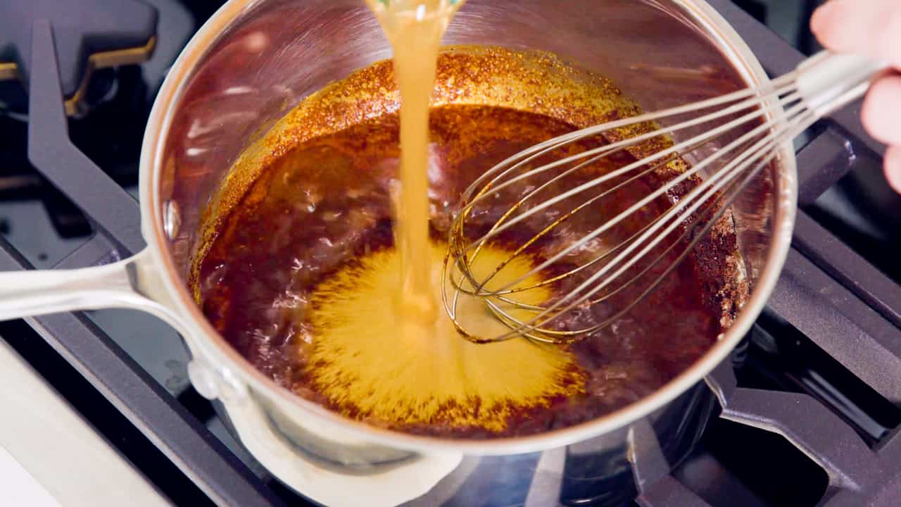  Vegetable broth being poured into a pot full of enchilada sauce ingredients. 