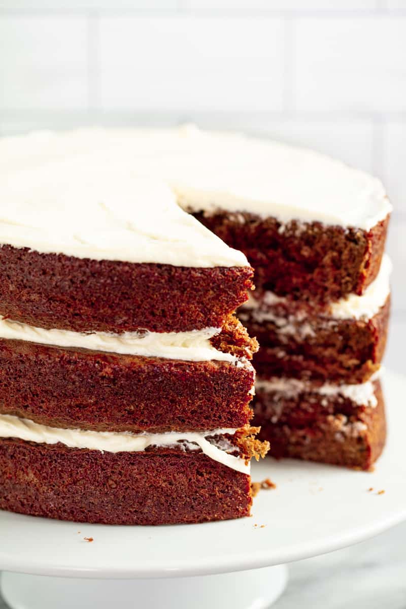 Red Velvet Cake with a slice taken out of it on a white cake stand.