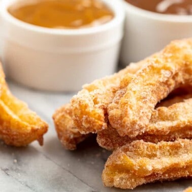 Angled view of Churros on a marble countertop with a bowl of caramel sauce and a bowl of chocolate sauce.