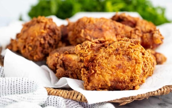 Angled view Crispy Fried Chicken on a paper towel on a wicker basket style platter.