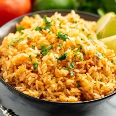 Angled view of Mexican rice and two lime wedges in a black bowl.