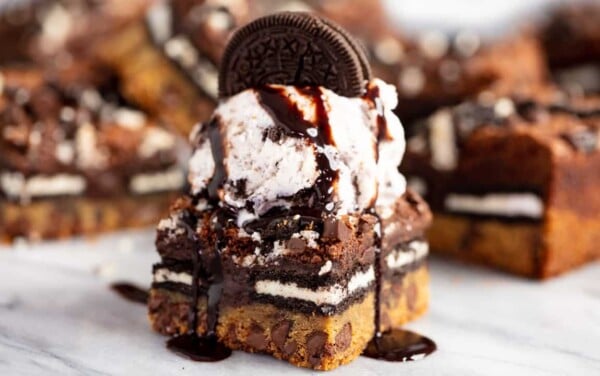 Close up of Slutty Brownies topped with a single scoop of vanilla ice cream and one whole Oreo cookie and drizzled with chocolate syrup.