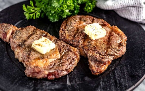 Angled view of Grilled Steak with a pad of butter on top served on a black plate.