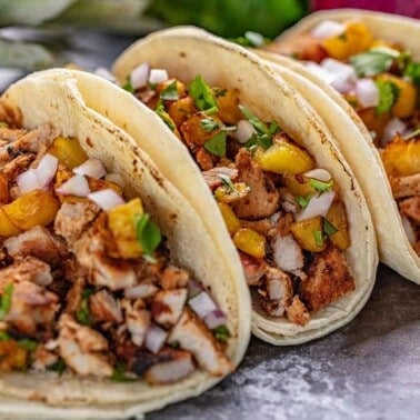 Angled view of Tacos Al Pastor on a black countertop.