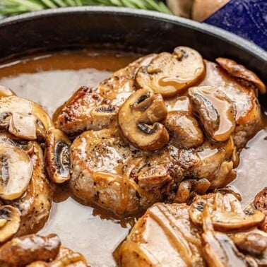 Smothered Pork Chops covered in mushrooms in a cast-iron skillet.