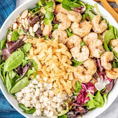 Bird's eye view of Thai Shrimp Salad topped with shrimp, crispy wonton strips, water chestnuts, slivered almonds, cilantro, and leafy greens in a white bowl.