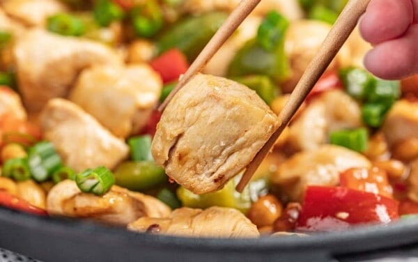 chopsticks holding up a piece of chicken in kung pao chicken