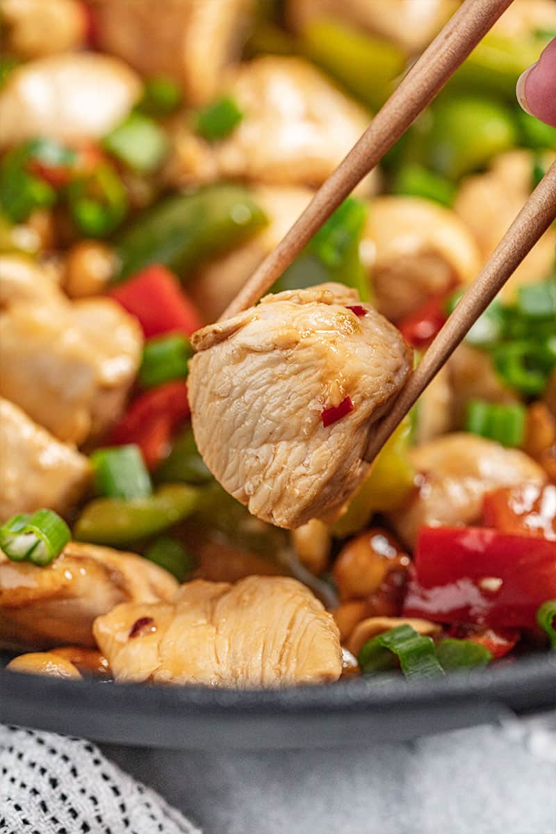 Chopsticks holding up a piece of kung pao chicken