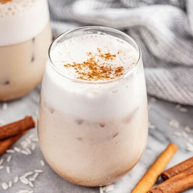 2 glasses of horchata surrounded by rice and cinnamon sticks