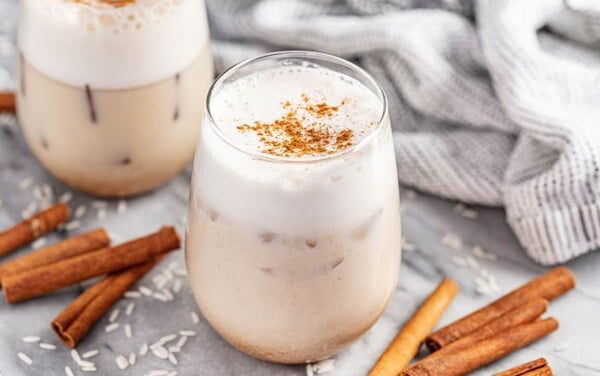 2 glasses of horchata surrounded by rice and cinnamon sticks