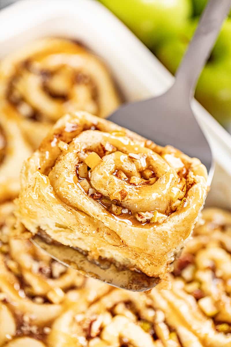 A close up view of a caramel apple cinnamon roll on a spatula