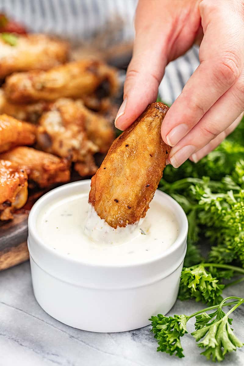 A hand dipping a chicken wing into ranch dressing