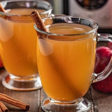 2 glass mugs full of apple cider with a cinnamon stick in each