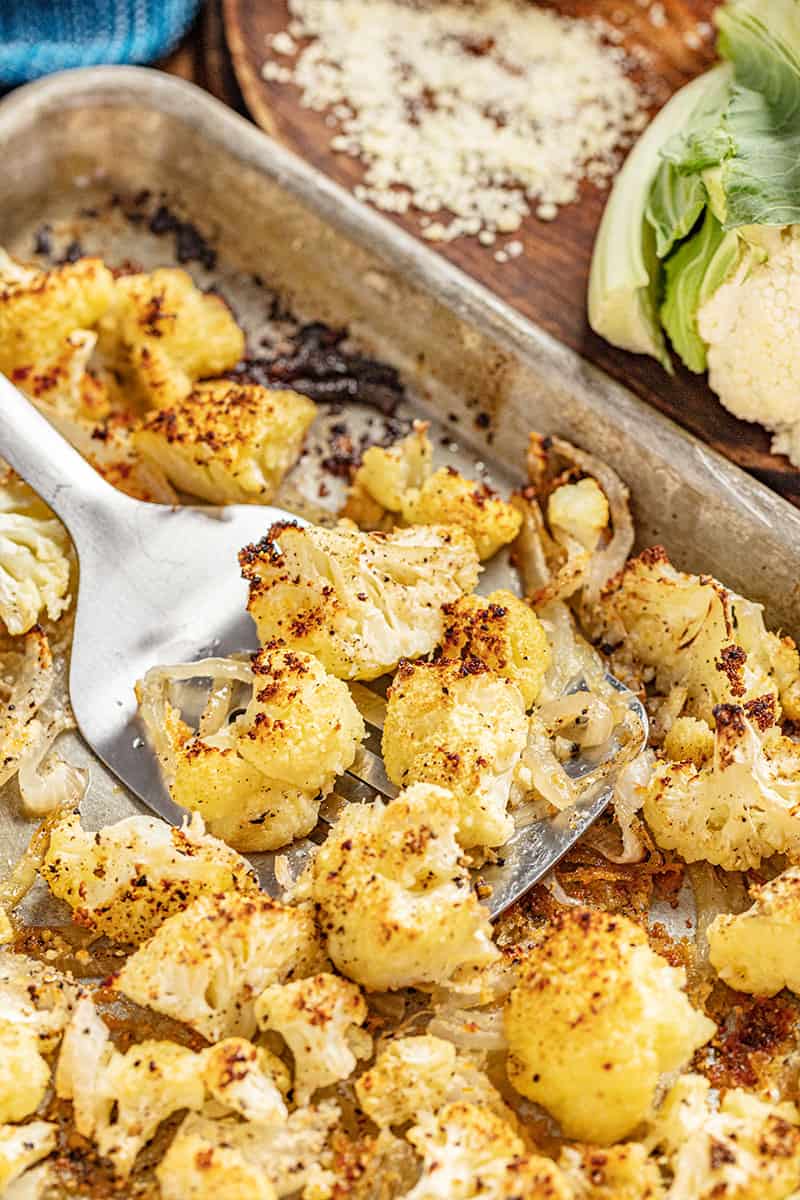 Close up view of a spatula holding up roasted cauliflower from a sheet pan.