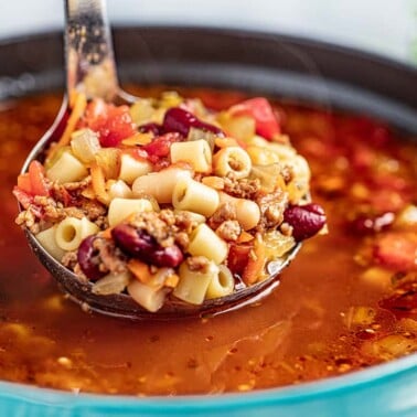 A ladle of pasta e fagioli held up over a stockpot.