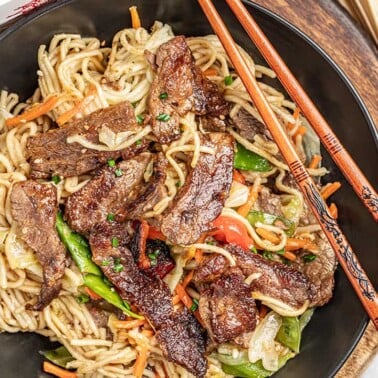 Overhead view of beef lo mein in a bowl with chopsticks.