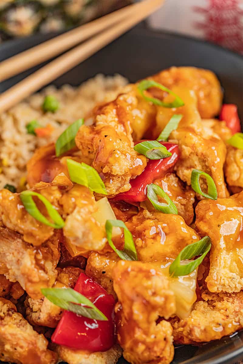 Close up view of sweet and sour chicken with sliced green onions on top.