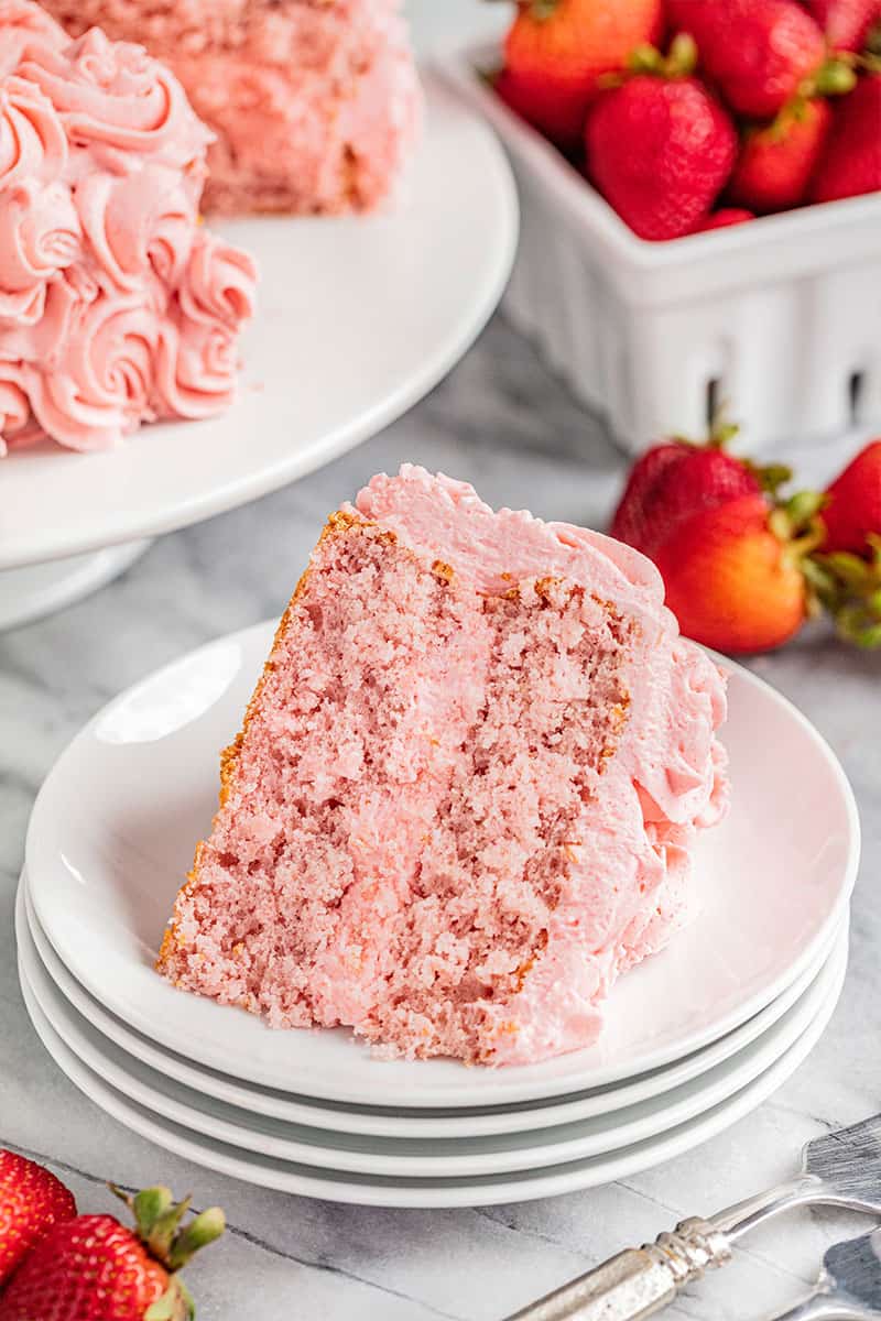 A slice of strawberry cake on a stack of small dessert plates.