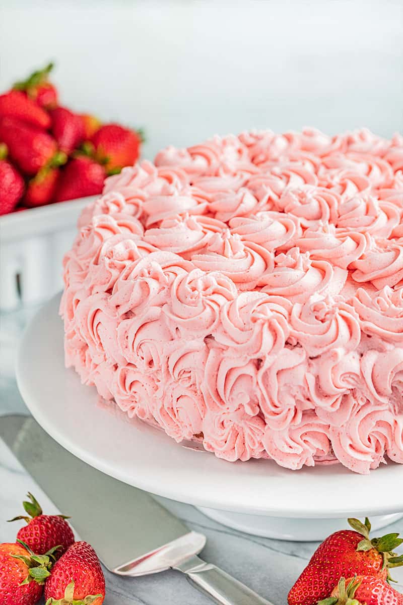 A whole strawberry cake on a cake stand.