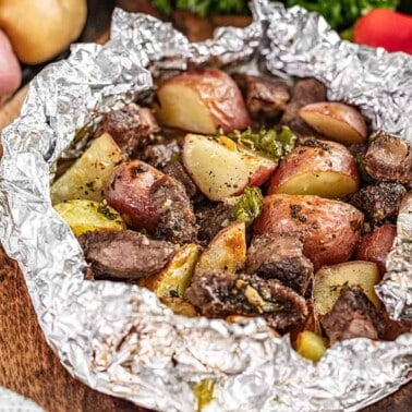 Seasoned steak and potatoes in an opened foil packet.