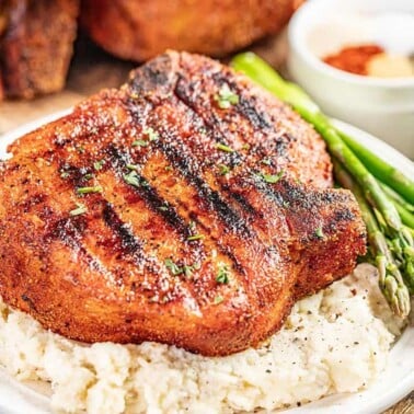 A large smoked pork chop on top of a bed of mashed potatoes on a plate.