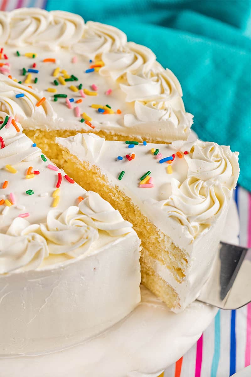 Removing a piece of cake from a whole homemade vanilla cake.