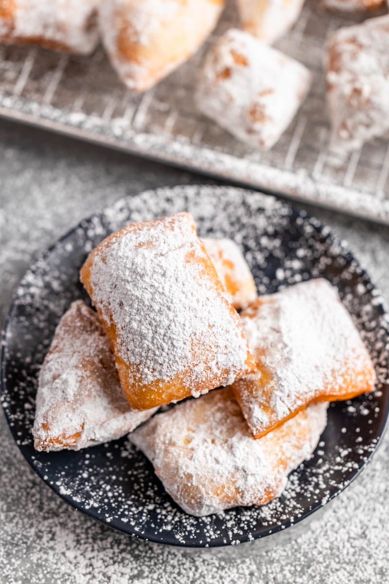 Overhead view of a pile of beignets on a dessert plate.