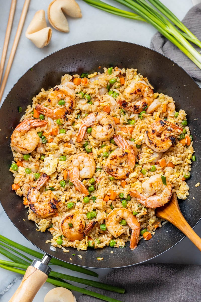 Overhead view of shrimp fried rice in a wok with a wooden spoon.